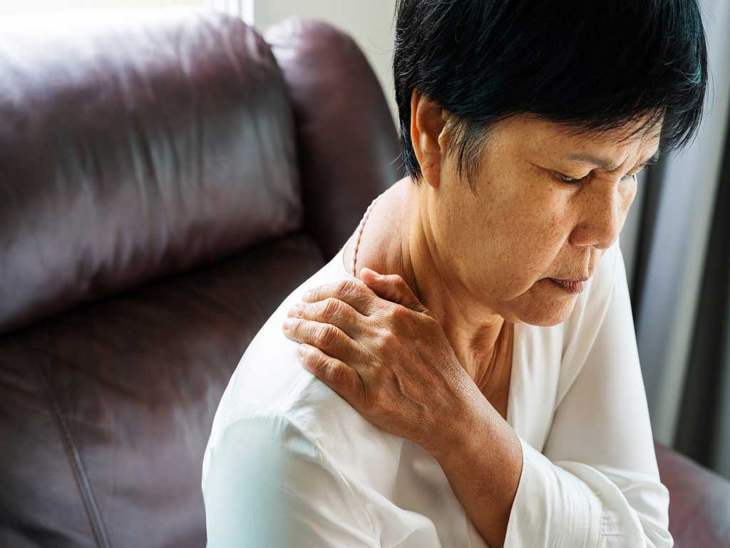 A woman sitting down and touching her shoulder due to pain