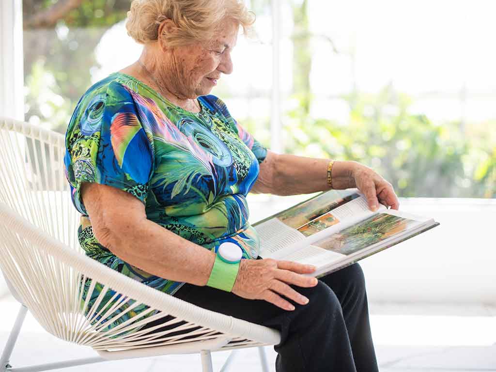 An elderly woman using TENS on her wrist while reading and sitting