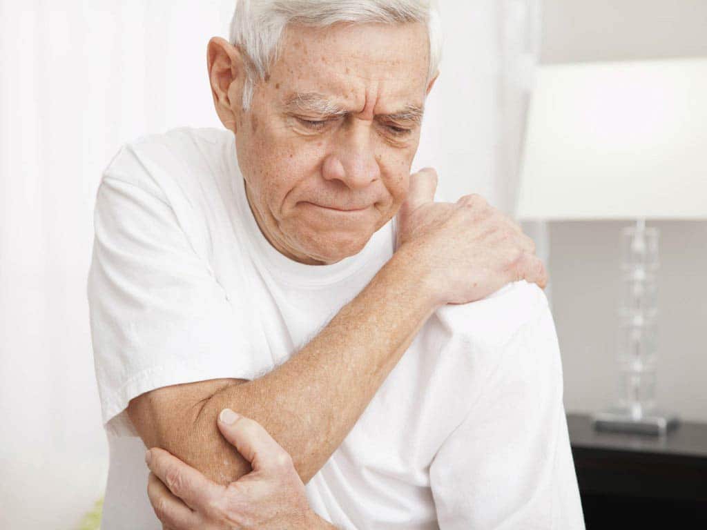 An elderly man touching his aching elbow and shoulder