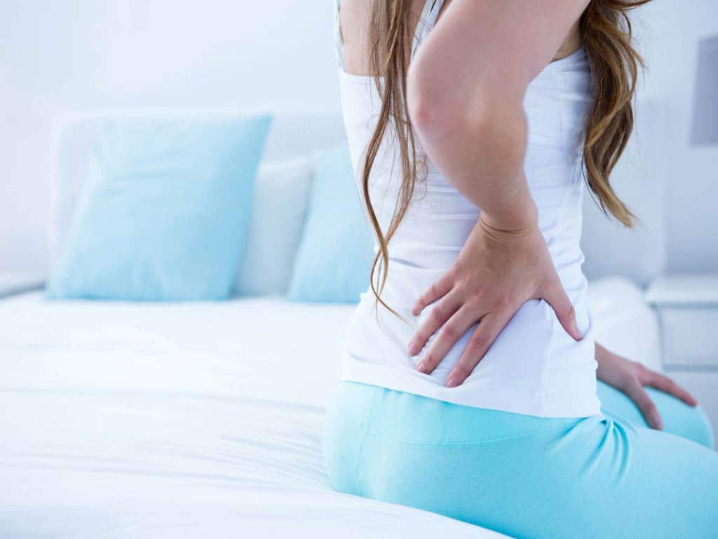 A woman sitting on a bed while touching her lower back