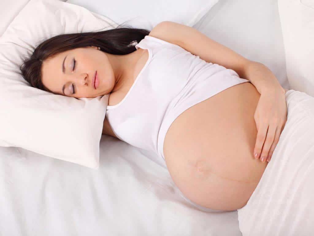 A pregnant woman sleeping on her bed.