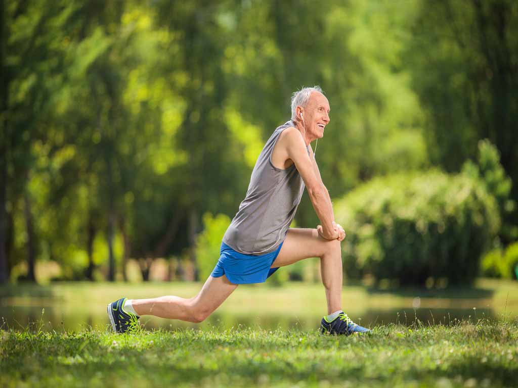 An elderly man performing outdoor stretching exercise.