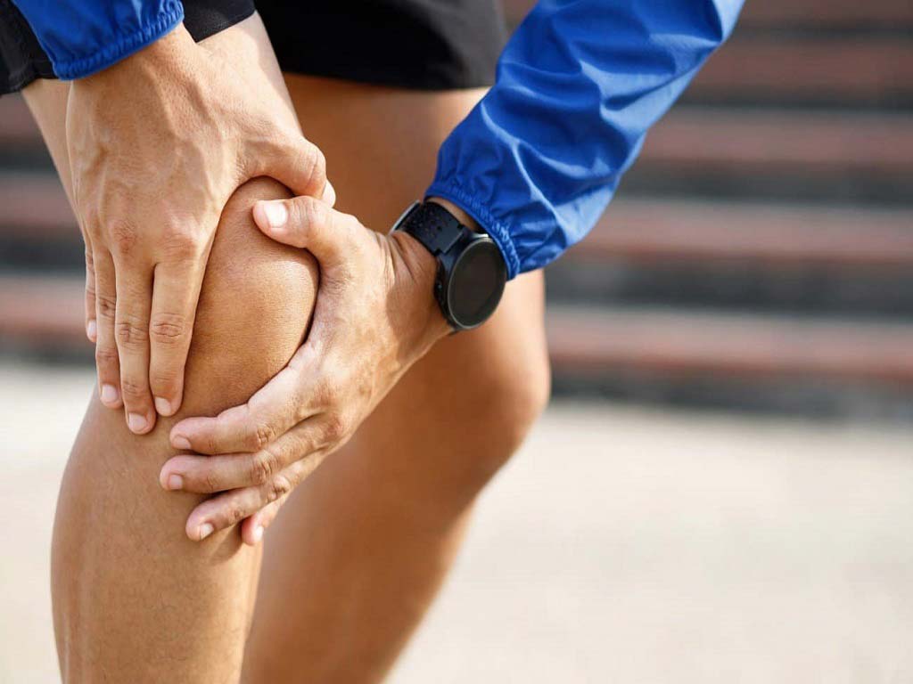 A person touching their aching knee with both hands