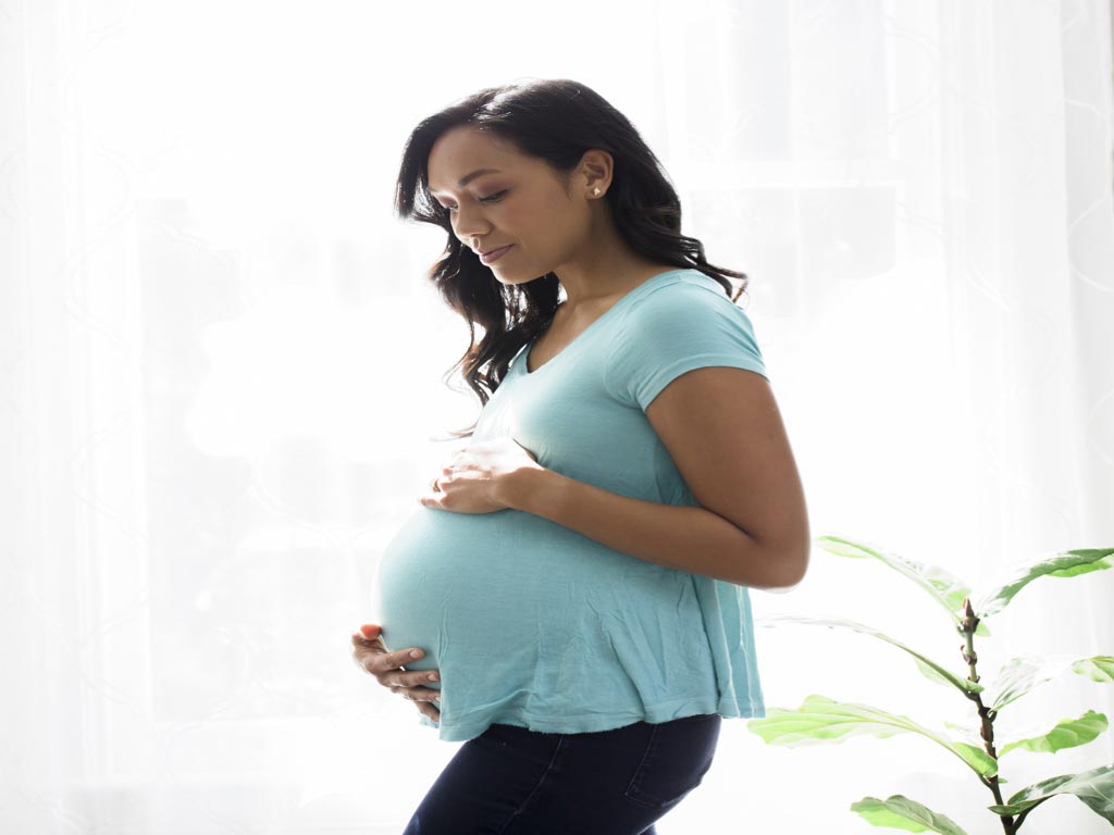 A pregnant woman standing while holding her abdomen
