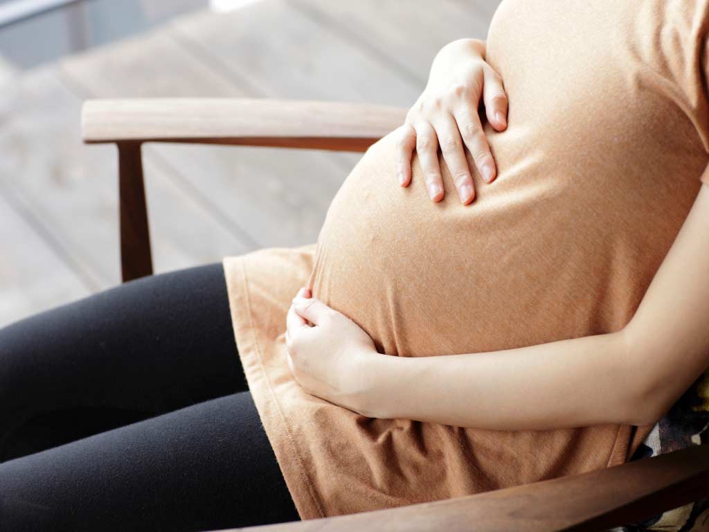 A pregnant woman sitting down in a chair while holding her abdomen
