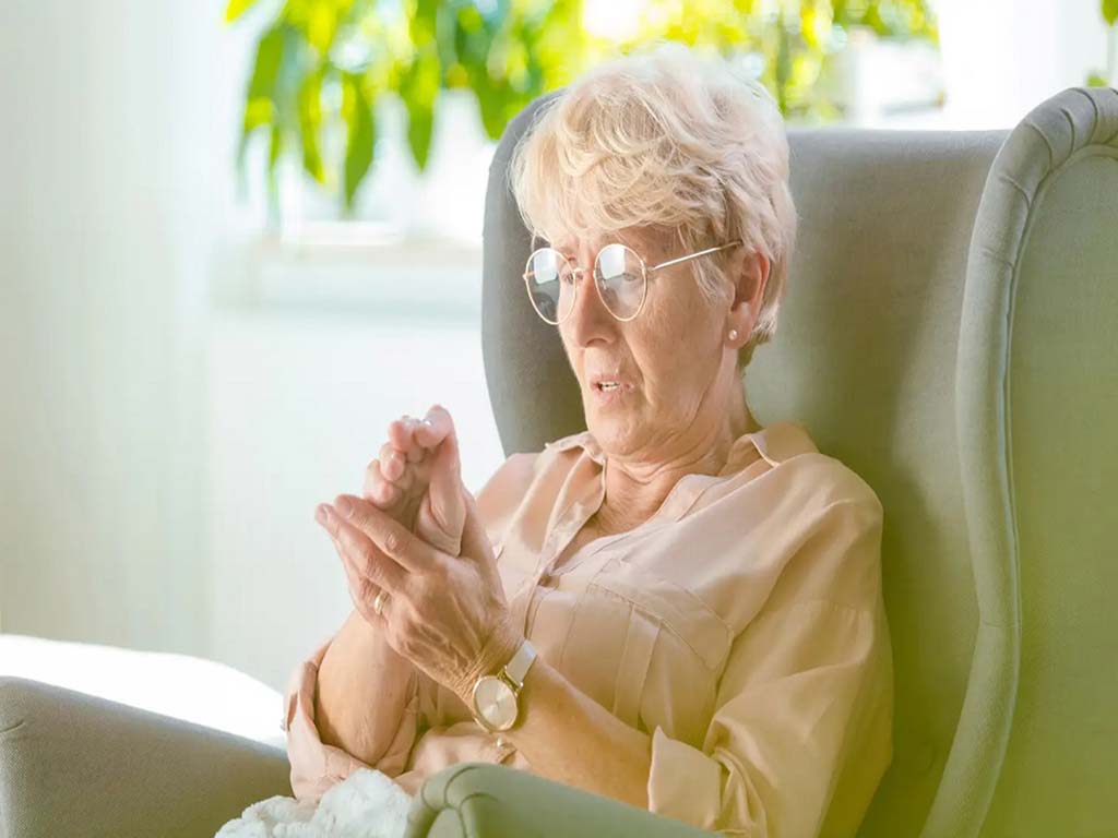 An elderly woman clutching her right hand in discomfort
