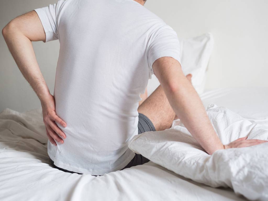 A man in bed touching his lower back due to pain
