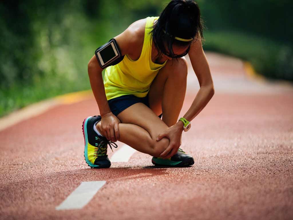 A track athlete touching her aching knee and ankle