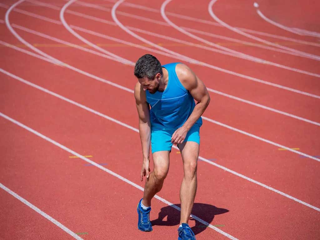 A man on the track field feeling discomfort in his calf.