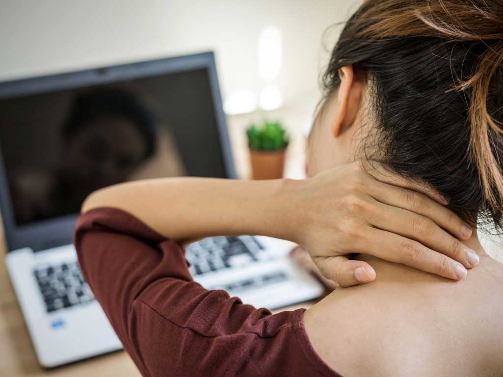 A woman holding the back of her neck in front of her laptop