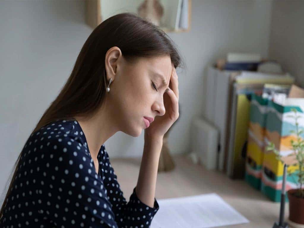 A woman closing her eyes while sitting in front of her desk