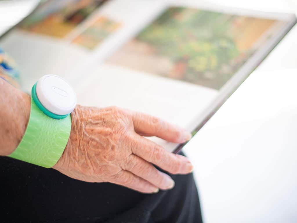 An elderly woman wearing iTENS on her wrist while reading a book