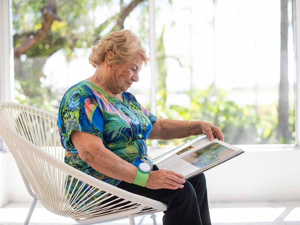 An elderly woman using TENS in her wrist while sitting and reading