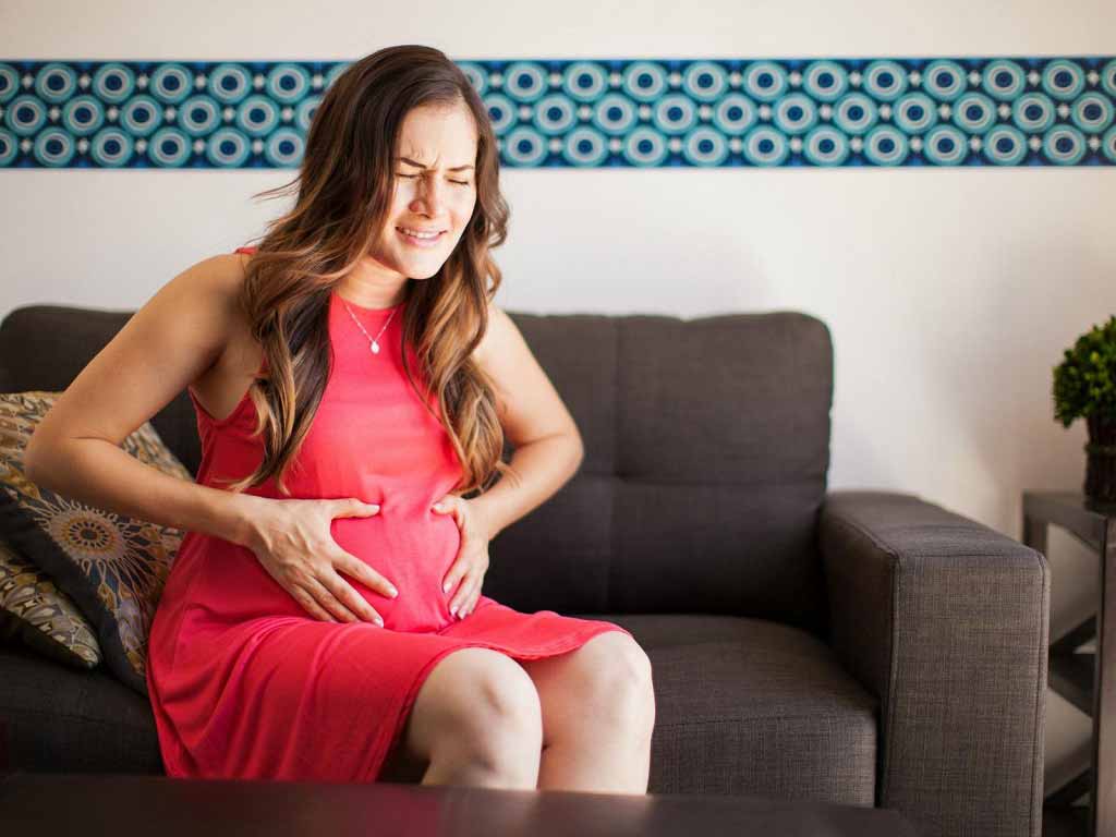 A pregnant woman sitting on a couch while touching her abdomen in pain