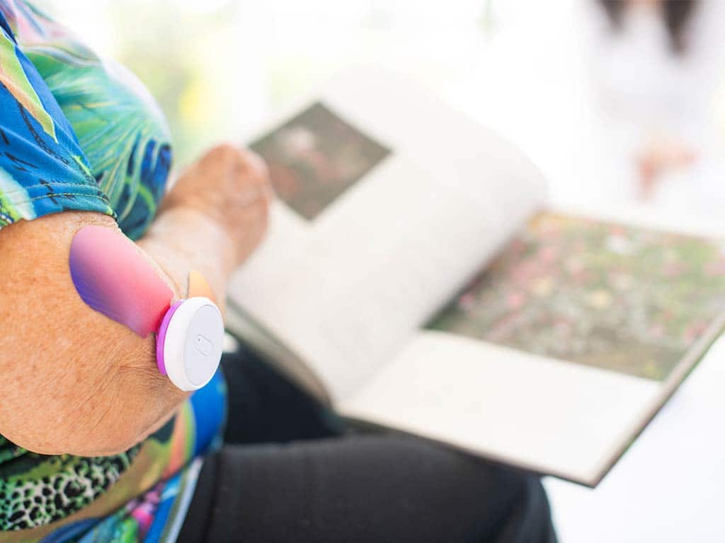 An elderly woman sitting while using TENS and reading a book