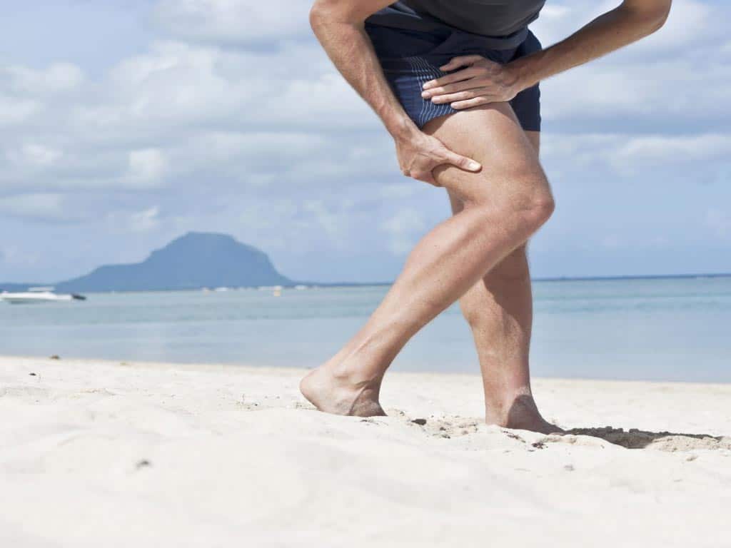 A man holding his hamstring at the beach