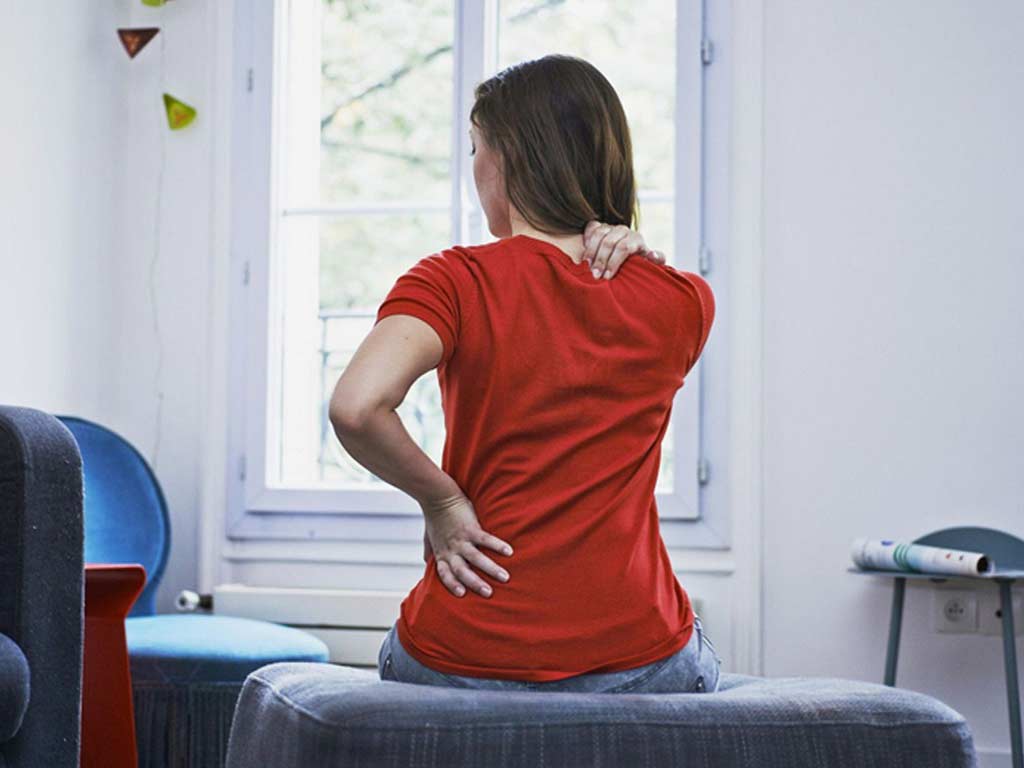 A woman touching her lower back and shoulder due to pain
