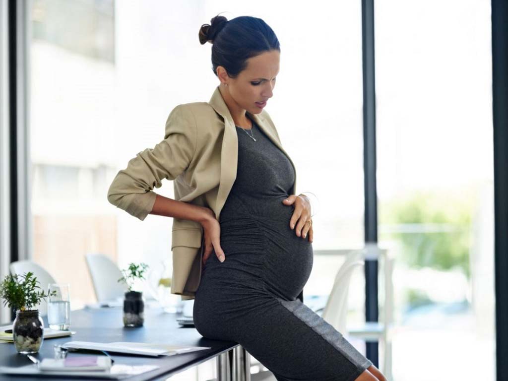 A pregnant woman sitting on a desk with her hand on her belly