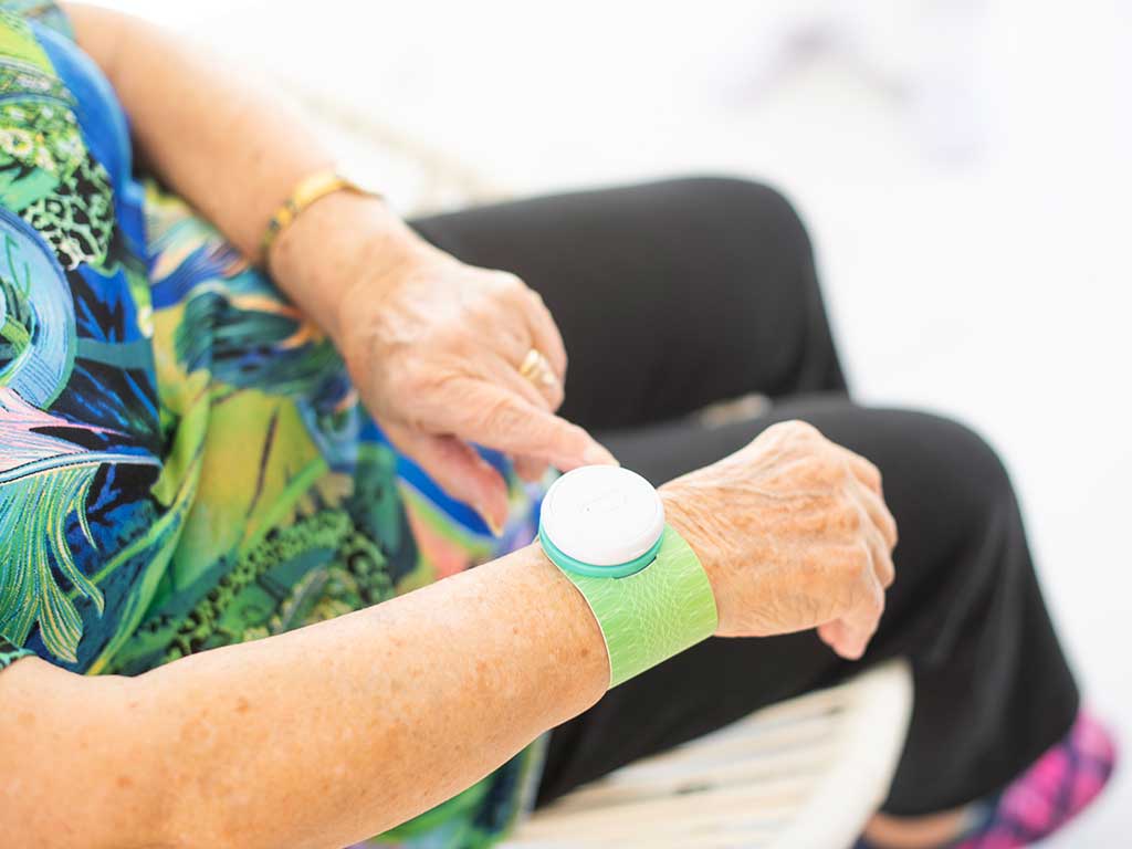 An elderly adjusting the TENS device settings on her arm