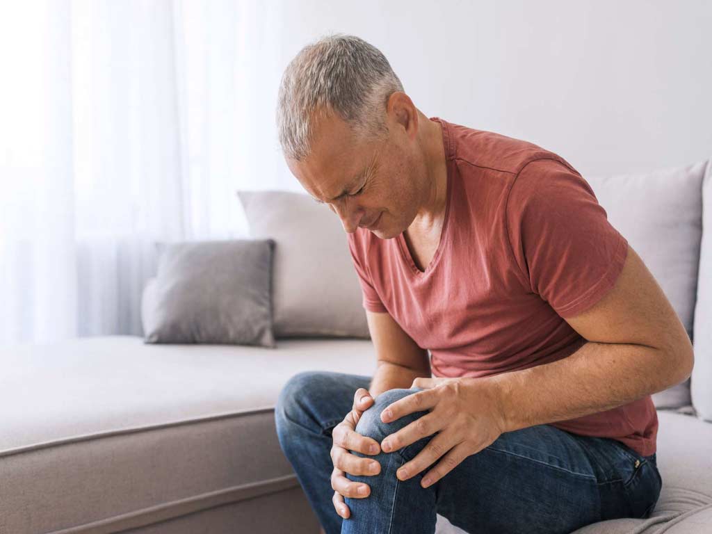 A man sitting on a couch while holding his painful knee