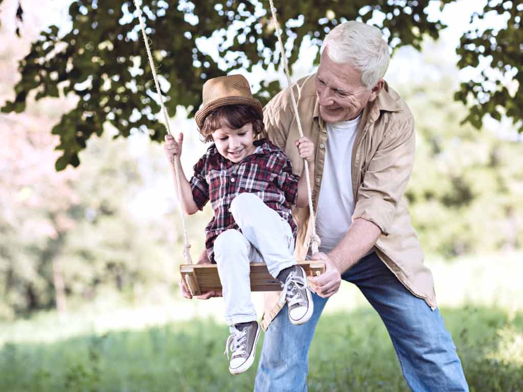 A grandfather pushing his grandson on the swing