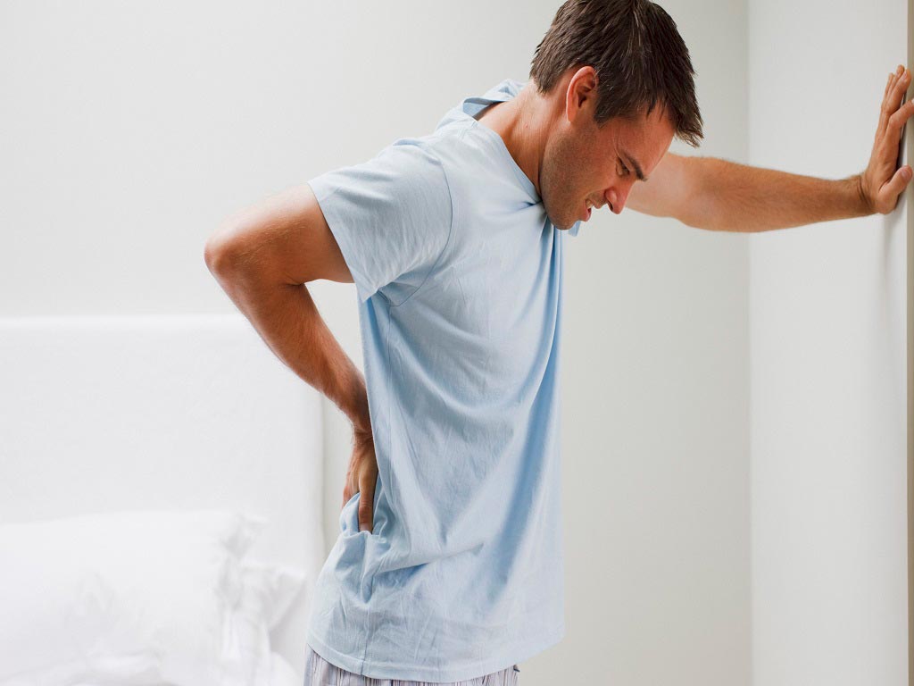 A man touching the wall and his lower back due to pain