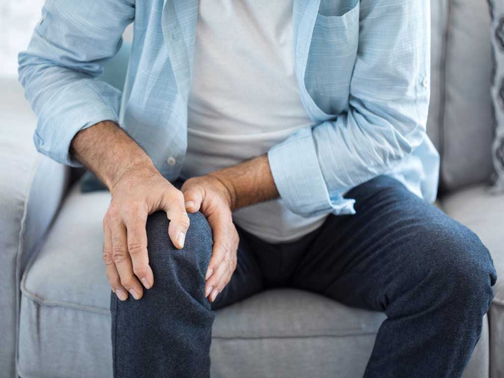 A man sitting on a couch while touching his painful knee