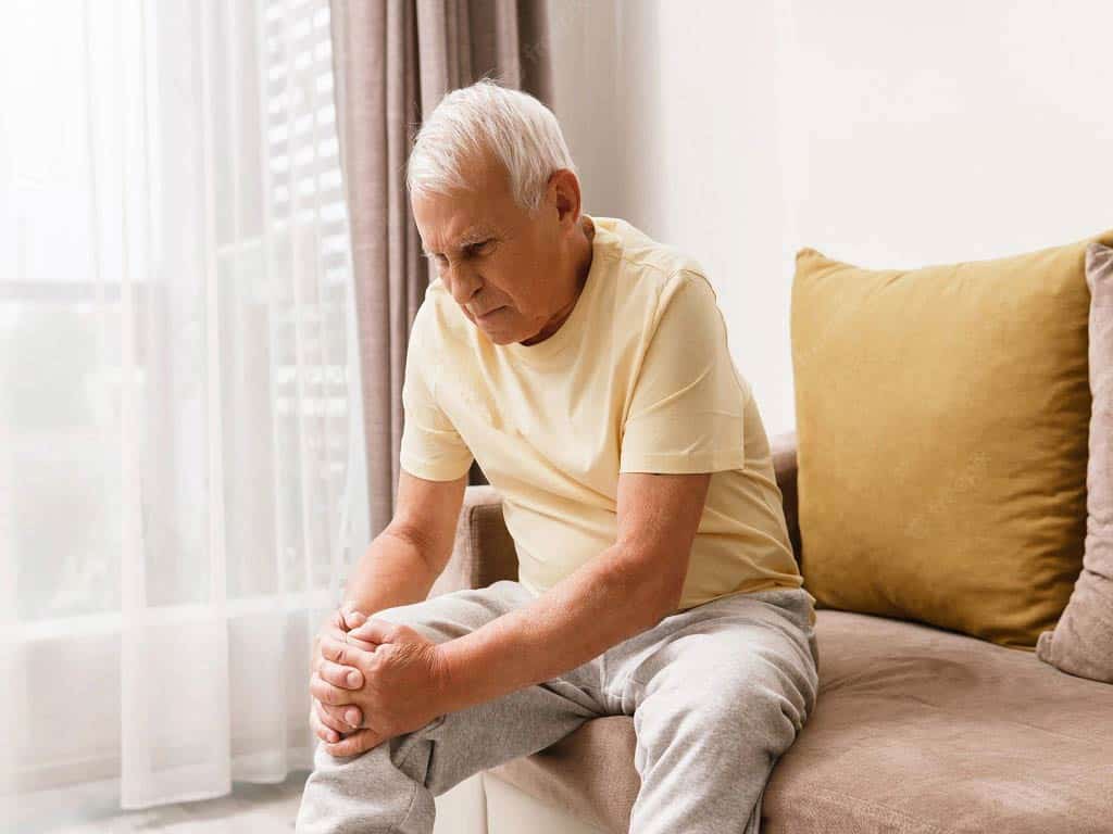 An elderly man suffering from knee pain while sitting