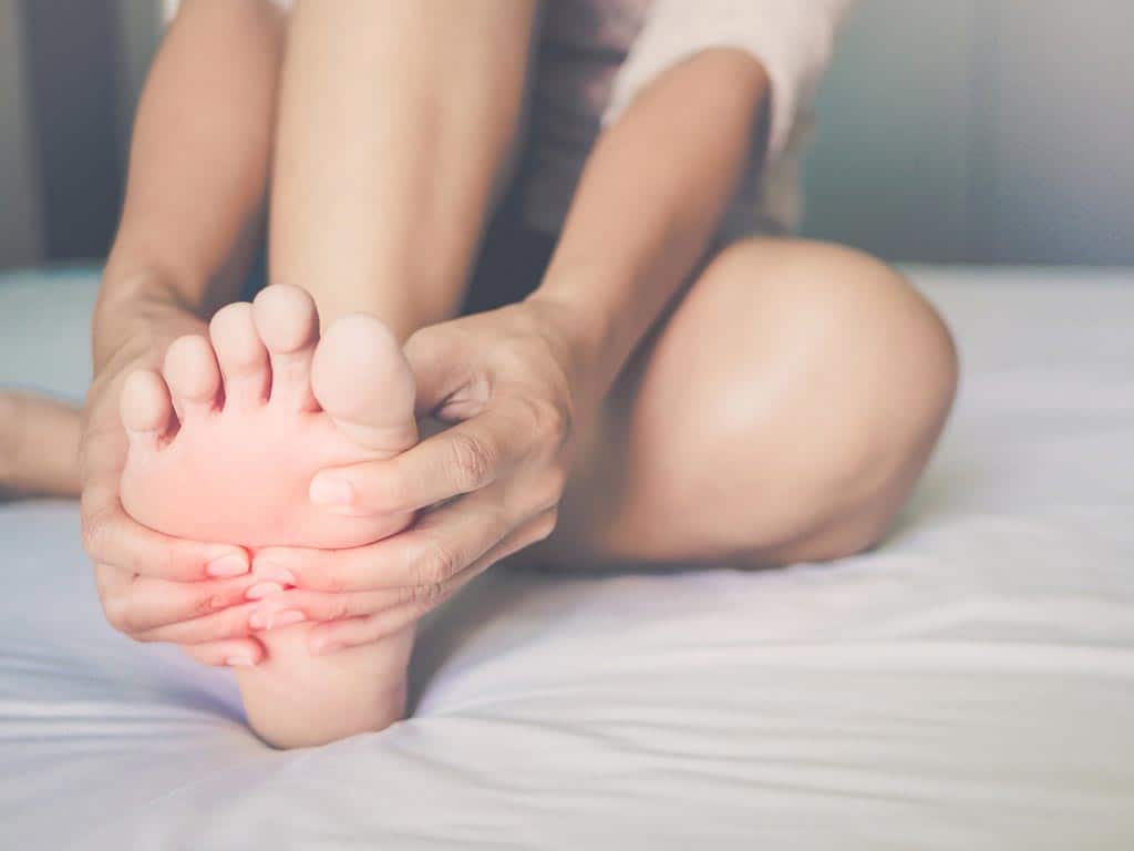 A female person holding her foot while on bed