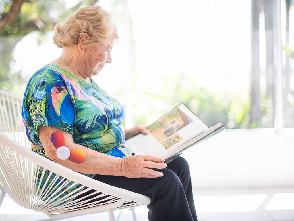 An elderly woman using TENS in the side of her elbows while sitting and reading