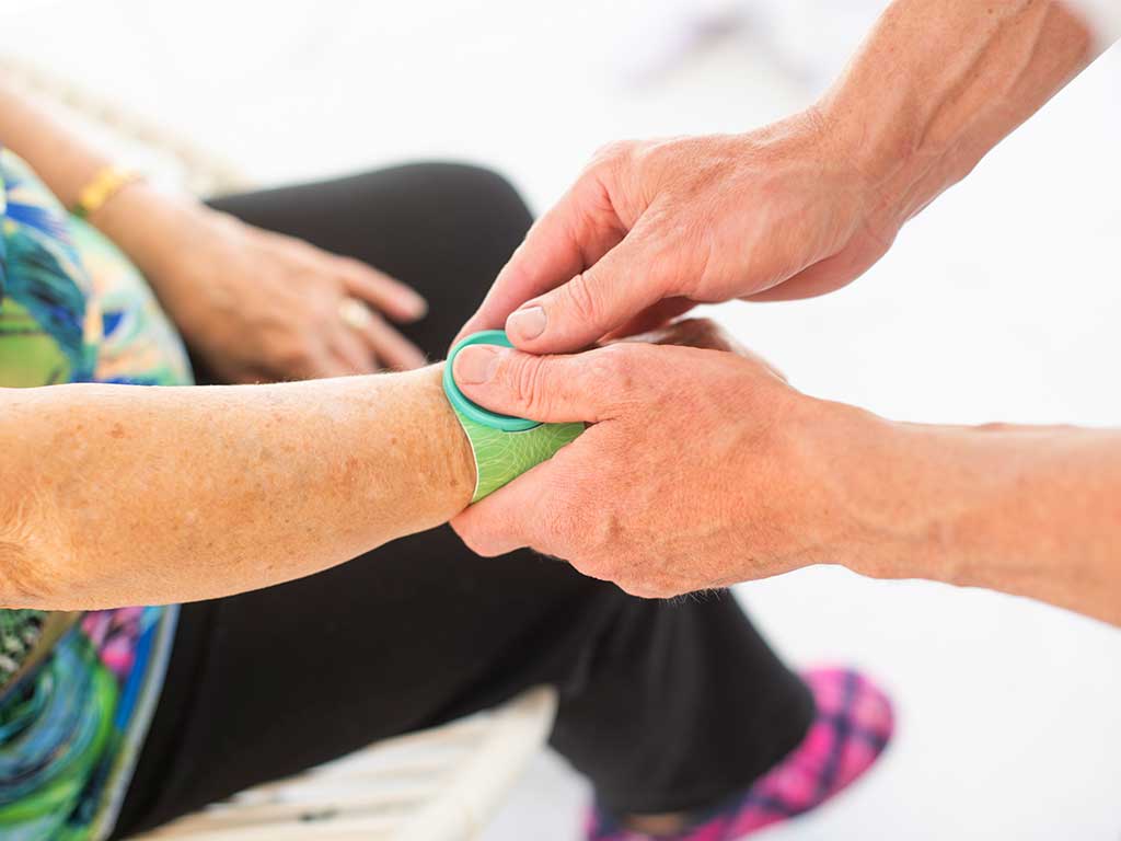 A person placing an iTENS unit on the wrist of an elderly woman