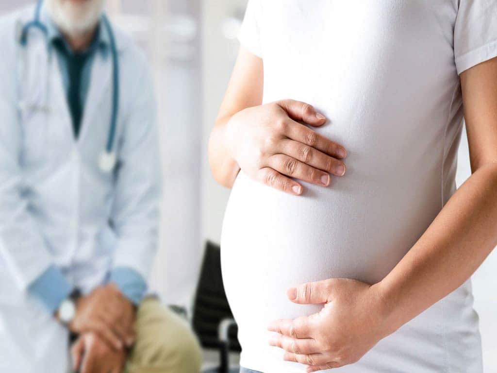 A woman at a clinic holding her bump with a doctor behind her