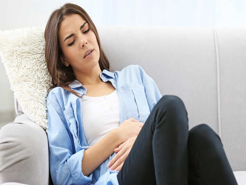 A woman sitting on a couch while touching her abdomen in pain