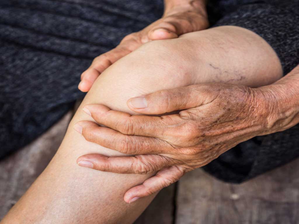 A elderly person holding their pained knee