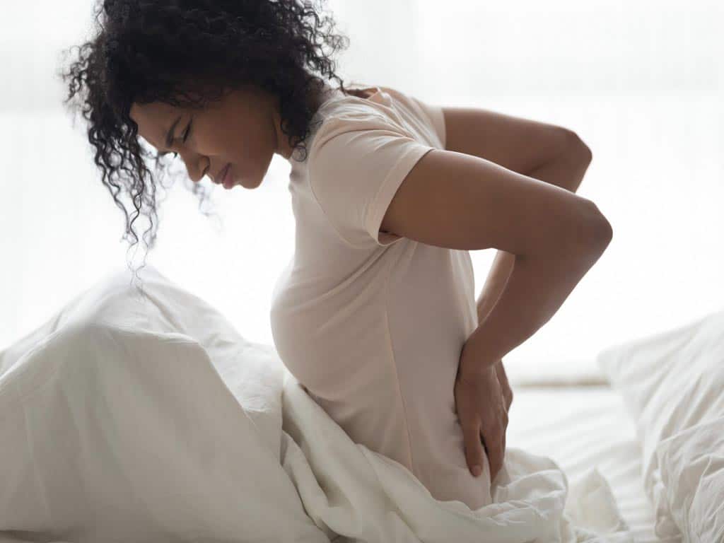 A woman suffering from back pain while sitting on a bed