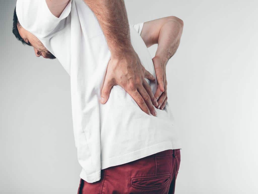 A man holding his lower back with both hands due to sciatica pain