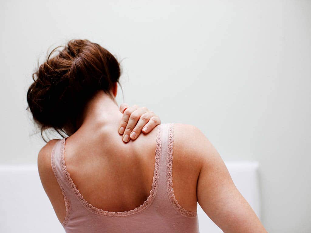A woman pressing the right side of her shoulder and neck
