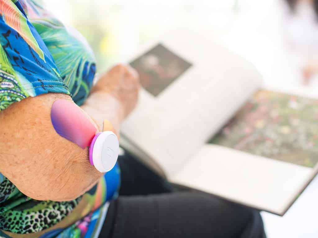 A woman using a TENS machine on her elbow while reading a book