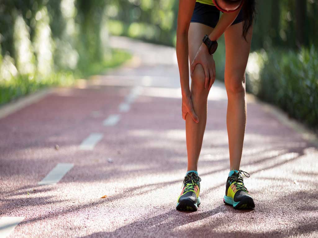 A woman experiencing leg cramps while running