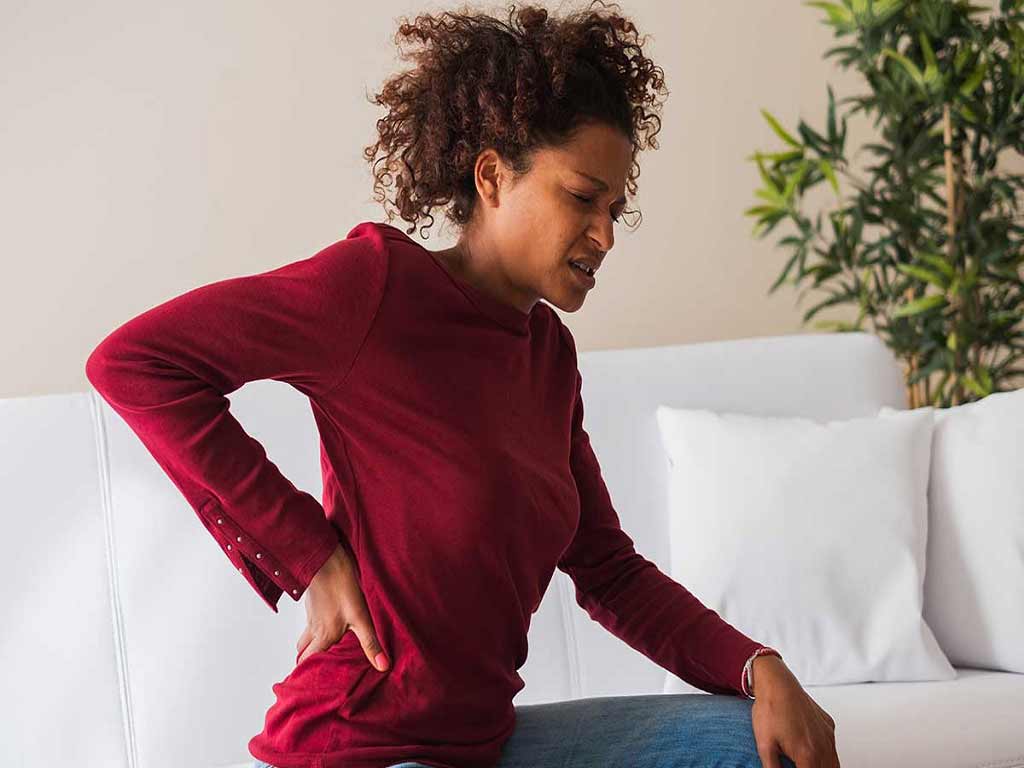 A woman experiencing lower back pain while sat on a sofa