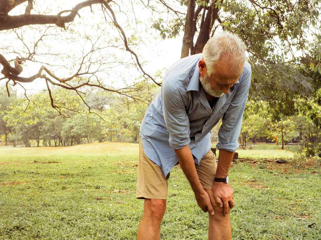 An elderly man with knee pain while outdoors