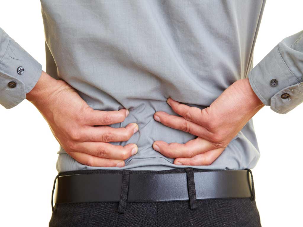 A person in a corporate attire touching their lower back with both hands due to pain