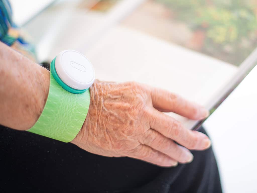 An elderly woman using an iTENS electrode on her wrist while reading