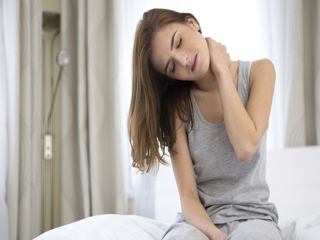 A woman sat in bed frowning due to neck pain